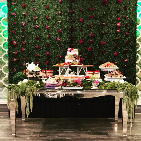 Dessert table with cakes, cupcakes, and pastries against a green wall with red flowers.