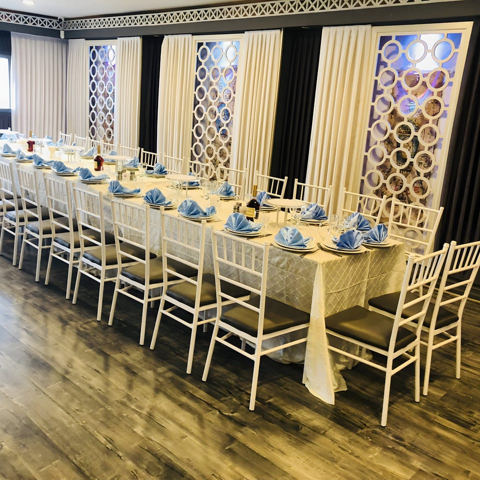 Long dining table set with white chairs, blue napkins, and wine bottles in a formal Fresco Ristorante setting.