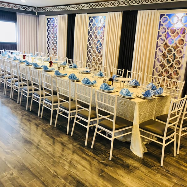 Long dining table set with white chairs, blue napkins, and bottles, ready for guests at Fresco Ristorante.