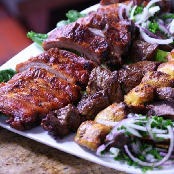 A platter of grilled ribs, meat chunks, and potatoes, garnished with red onion and parsley.