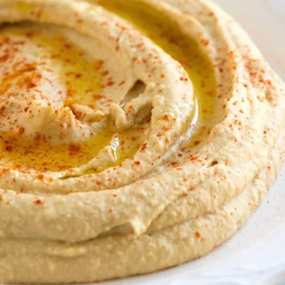 Creamy hummus drizzled with olive oil and sprinkled with paprika, served on a white plate.