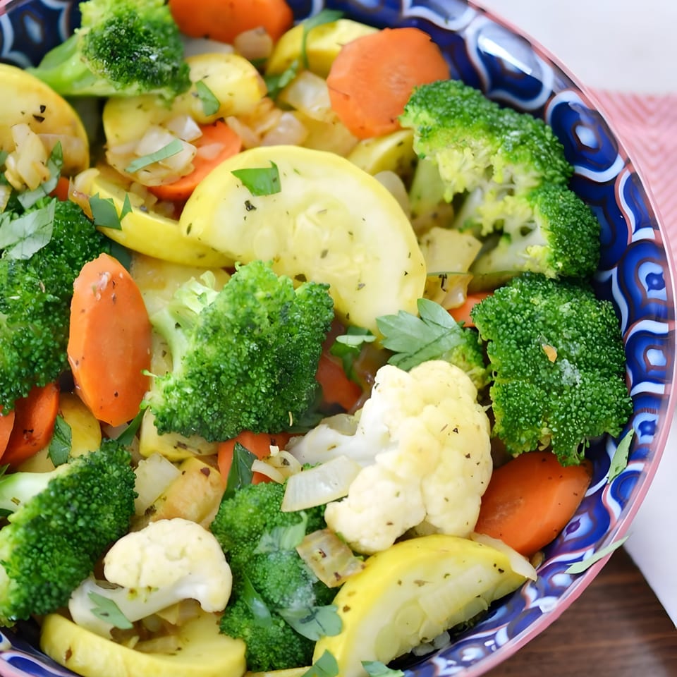 A colorful bowl of steamed vegetables, including broccoli, cauliflower, carrots, and yellow squash.