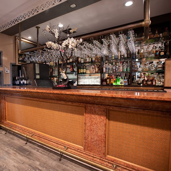 Fresco Ristorante's bar with a wooden counter, glass racks, and bottles of liquor on shelves.